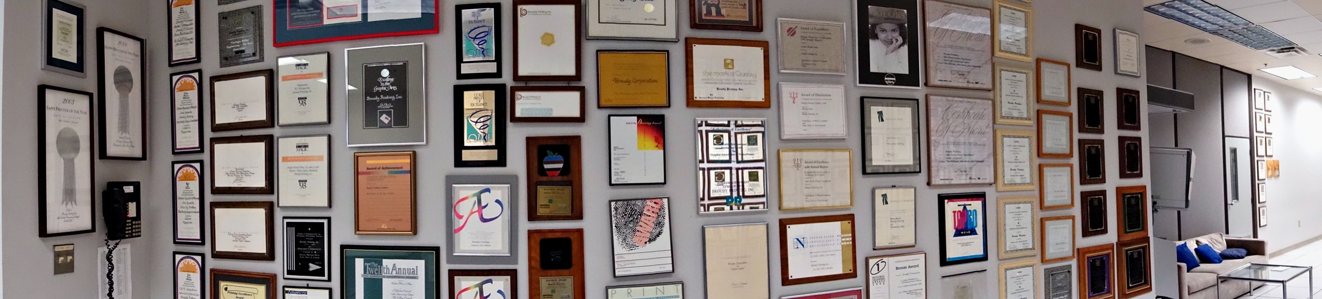 A panorama of one wall of the Broudy Printing awards room, covered end to end with framed printing awards
